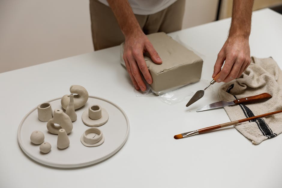 Close-up of hands sculpting clay with tools in a studio setting.
