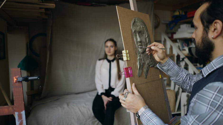 Artist creating a clay portrait in a studio, with model posing in background.